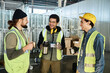 © pressmaster - Three young cheerful engineers in workwear looking at each other while discussing something funny and having hot tea at break in warehouse