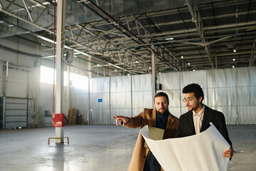 Leinwandbilder - Young confident entrepreneur pointing forwards while explaining sketch or building plan on blueprint to colleague at working meeting in warehouse