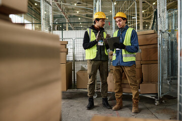 Leinwandbilder - Young confident enginner in protective hardhat and reflective vest explaining something to colleague with tablet at working meeting