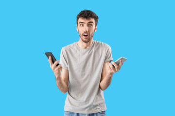 Wall Mural - Surprised young man with mobile phones on blue background