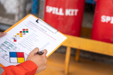Wall Mural - action of safety officer is checking chemical hazard material form for correct the oil spill kit whi