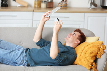 Sticker - Handsome young man with credit card and tablet computer lying on sofa while shopping online