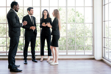 diversity group of businesspeople strictly dressed in the suits standing meeting by office window. a