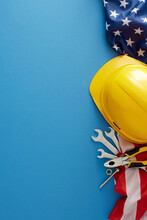 Embrace The American National Holiday: Labor Day. Top View Vertical Shot Of American Flag, Safety Helmet, Tools On Blue Background With Empty Space For Advert Or Text