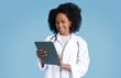 © Prostock-studio - Happy black millennial lady doctor in white coat making notes in tablet, use app for chat
