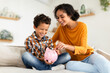 Happy Mom And Little Son Putting Coin In Piggybank Indoor