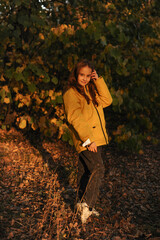 a cute girl dressed in a yellow jacket and with loose hair walks in the forest in late autumn