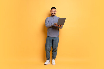 Excited Young Asian Man With Laptop Computer Posing Over Yellow Studio Background