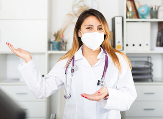 Wall Mural - Young mexican female doctor in medical mask inviting to doctor's office