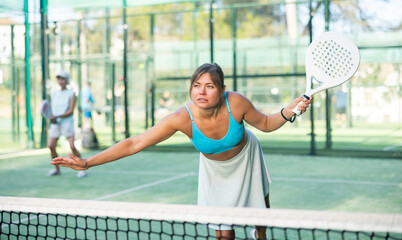 Wall Mural - Young woman in skirt playing padel tennis on court. Racket sport training outdoors.