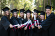 © Михаил Решетников - Row of happy young people in graduation gowns holding diplomas outdoors.