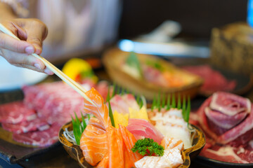 Wall Mural - Close up of woman hand uses chopsticks to put salmon sashimi on a plate in a Japanese restaurant..