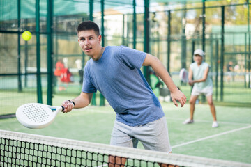 Wall Mural - Caucasian teenage boy in sportswear playing padel tennis match during training on court.