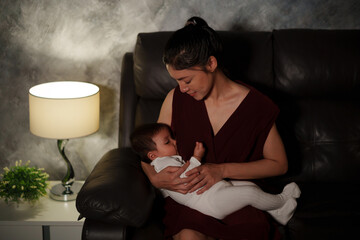 Wall Mural - happy mother breastfeeding infant baby on sofa in the living room at night