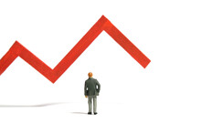 Miniature Tiny People Toy Figure Photography. Investment Failure And Loss Concept. A Businessman Standing In Front Of Red Bar Declining Graph. Isolated On A White Background