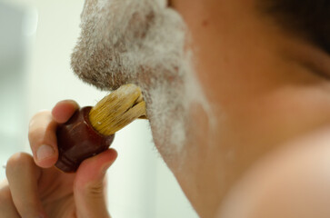 Close up of a man applying shaving cream with a brush to his beard