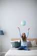 Joyful woman with a globe on the bed in the living room having fun.