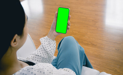 Poster - Mockup image of asian woman holding black smartphone with blank green screen at home.