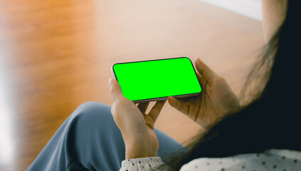 Poster - Mockup image, a woman holding black smartphone with blank green screen at home or office