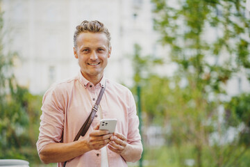 Happy man, satisfied mobile phone customer, smiling on city street. Engaged in mobile communication, he texts message or uses mobile app, reflecting seamless integration of technology into daily life