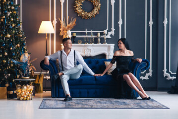 Poster - Portrait of a young couple in their living room at christmas eve.
christmas decoration on a sofa. Lovely couple in love sitting on the couch and holding hands near christmas tree