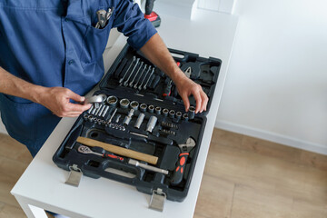 Close up of professional handyman in uniform with open tool bag sitting on home kitchen floor 