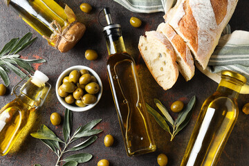 Bottles of olive oil, olives and slices of bread on gray background, top view