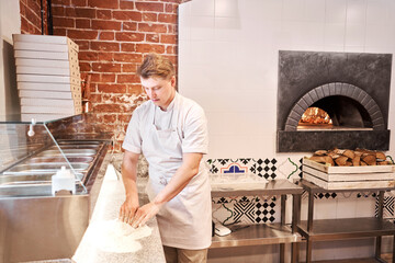 Wall Mural - The chef prepare pizza. Raw pizza ready to bake. Cook in a apron in the kitchen Rolls out pizza dough. boxes for food delivery on background.