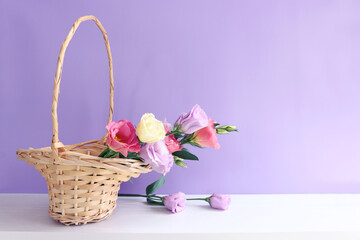 Wall Mural - image of delicate pink flowers in the wicker basket over wooden table and purple background