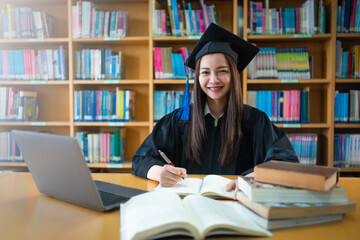 Wall Mural - Portrait young happy and excited Asian woman university graduate in graduation gown and cap in the library. Education stock photo