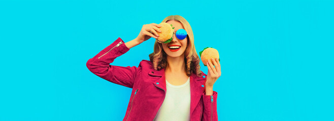 Wall Mural - Portrait of stylish modern laughing young woman with burger fast food on blue studio background