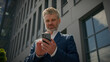 © Yuliia - Middle-aged man senior mature business employer businessman happy smiling mobile phone chatting app smartphone browsing check crypto in cellphone order taxi in city near office building bottom view