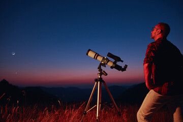 Wall Mural - astronomer looking at the starry skies and crescent moon with a telescope.