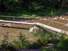 Wooden Bridge Over River With Turquoise Waters And Rocky Riverbed In The Forest Of Ukraine. Mountain Stream Flowing Through A Forest, A Small Wooden Bridge On A Hiking Trail Crossing The River.