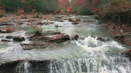 Wall Mural - Drone flys over Arkansas ozark mountain creek cascade lined with colorful forest trees in fall along river rocky coastline. 