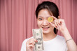 Portrait of a smiling Asian woman wear white shirt and holding banknotes or money us dollar and bitcoin BTC included with Cryptocurrency hand picked on pink background.