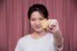 Portrait of a smiling Asian woman wear white shirt and holding banknotes or money us dollar and bitcoin BTC included with Cryptocurrency hand picked on pink background.