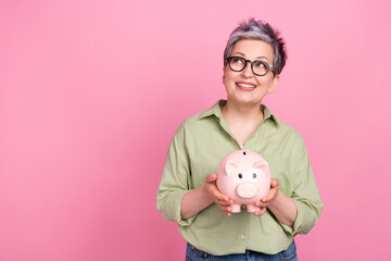 Photo of dreamy pensioner business lady khaki trendy shirt hold piggy bank look empty space earn money isolated on pink color background