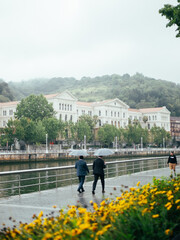 Wall Mural - two people with umbrellas walking in front of the University of Bilbao, Spain