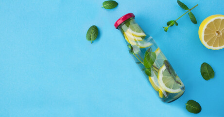 Wall Mural - Detox or infused water with lemon and mint in the glass bottle on the blue background. Top view. Copy space.