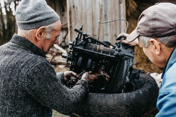 Wall Mural - elderly man tuning a car engine at home in a garage, customizing an engine in a village.