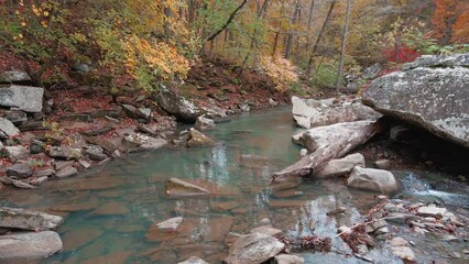 Wall Mural - Slow aerial flight over blue Arkansas ozark mountain creek in fall with autumn colored forest and rocky riverbed