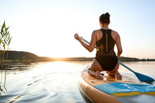 Woman Paddle Boarding On SUP Board In River At Sunset, Back View