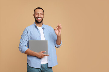 Poster - Smiling young man with laptop showing OK gesture on beige background, space for text