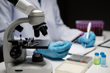 Wall Mural - Scientist hand taking a sample tube from a rack with machines of analysis in the lab background, Technician holding tube test in the research laboratory.