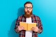 Photo of amazed funny young student guy beard glasses holding orange copybook shocked reaction organizer isolated on blue color background