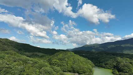 Wall Mural - Drone shot over green forested hills under cloudy sky, time lapse