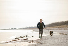 Middle Aged Caucasian Man Walking His Border Collie Dog On A Winter Beach