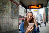 Fototapeta Fototapeta Londyn - Young caucasian woman using a smart phone while waiting for a bus at the bus stop in London UK