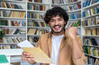 © Liubomir - Portrait of young successful student, man received letter of notification of good results of interview exam, hispanic man joyfully looking at camera inside library, holding mail envelope.